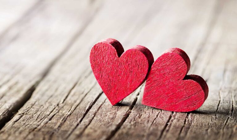 Two small red wooden hearts propped up against each other on a wooden surface